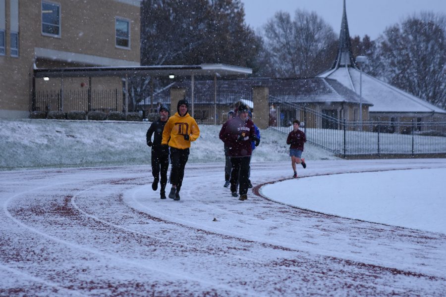 A group of runners led by Assistant Varisty Track Coach teacher Adam Boehm, run on a snowy day.