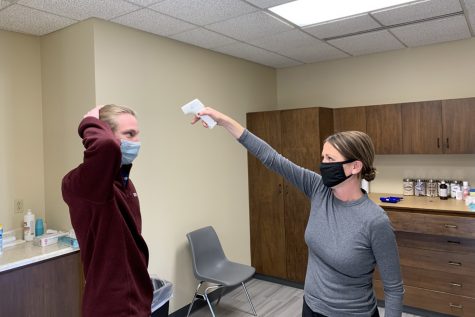 Nurse Molly Deveruex tests Senior Ryan Flavin's temperature.