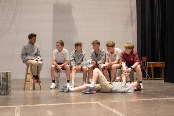 Middle schoolers group together in between acts at a rehearsal, engaging in conversations and awaiting their next lines.